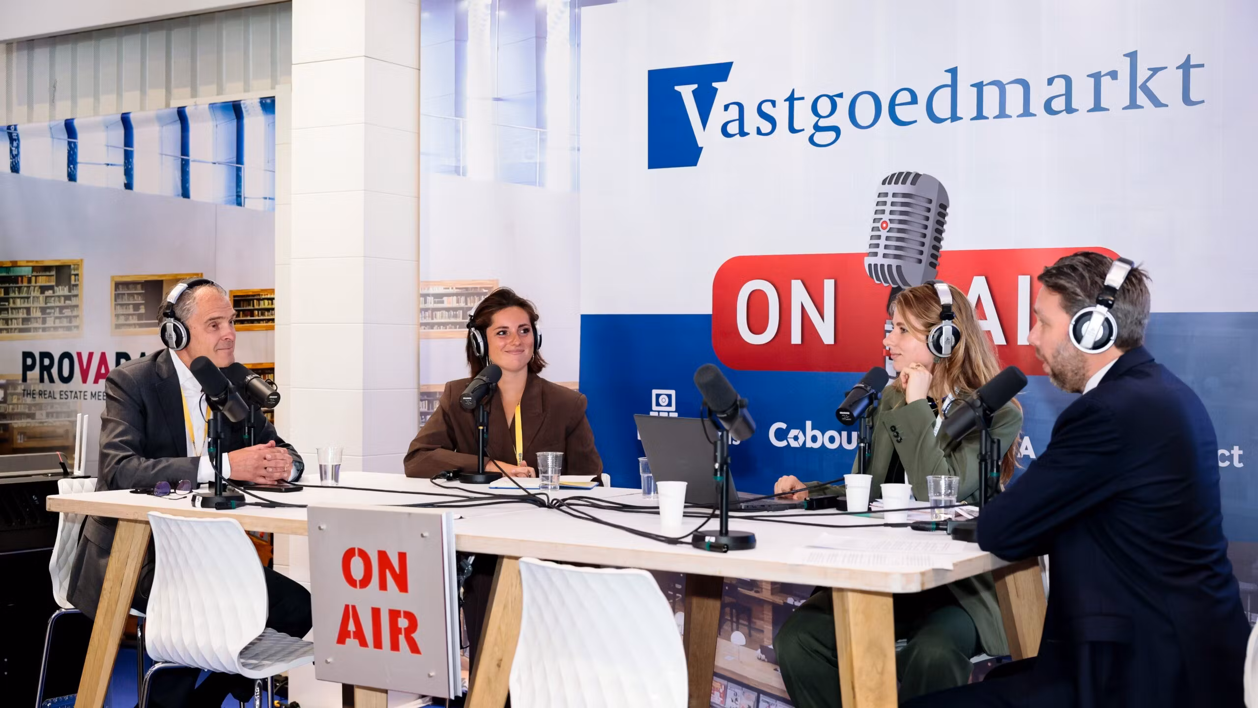 “Radiostand op beursvloer met podcastmicrofoons, koptelefoons en tv-scherm voor dagprogramma”